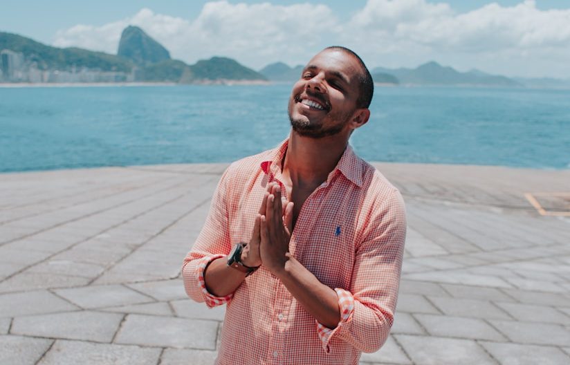 man in pink dress shirt standing on gray concrete pavement near body of water during daytime